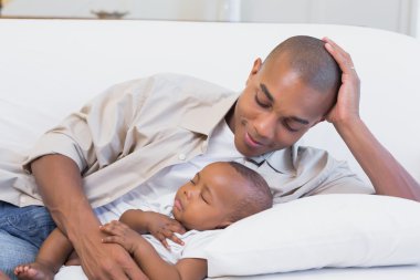 Happy young father with baby son on couch clipart