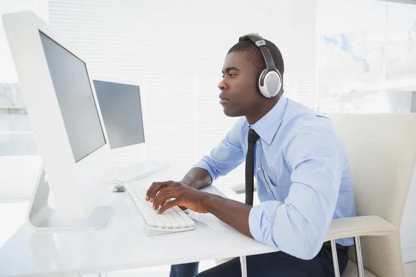 Konzentrierter Geschäftsmann, der an seinem Schreibtisch Musik hört — Stockfoto