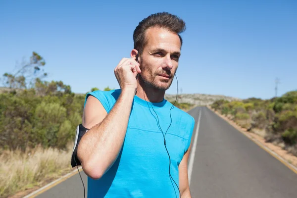 Athletic man adjusting his earphones on a run — Stock Photo, Image