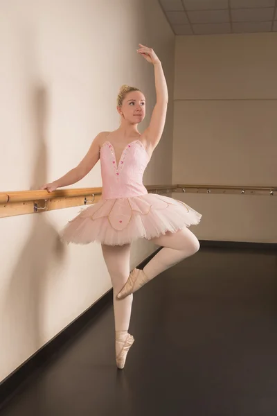 Прекрасная балерина, стоящая на пуантах, держа барре — стоковое фото