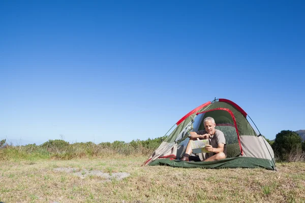 Happy camper looking at map sitting in his tent — Stock Photo, Image