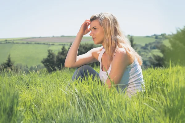 Hezká blondýnka myšlení a sedí na trávě — Stock fotografie