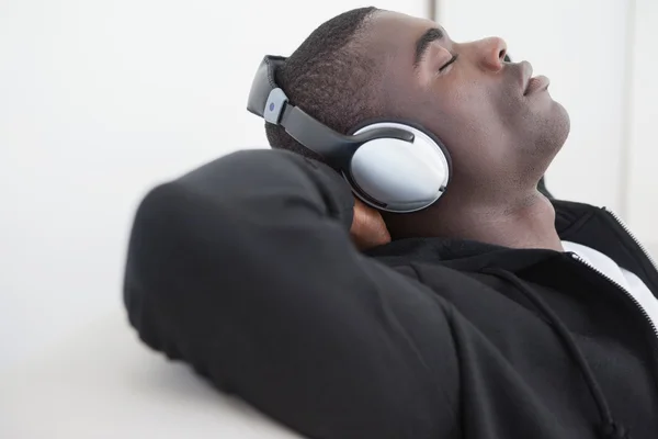 Casual homem sentado no sofá desfrutando de música com os olhos fechados — Fotografia de Stock