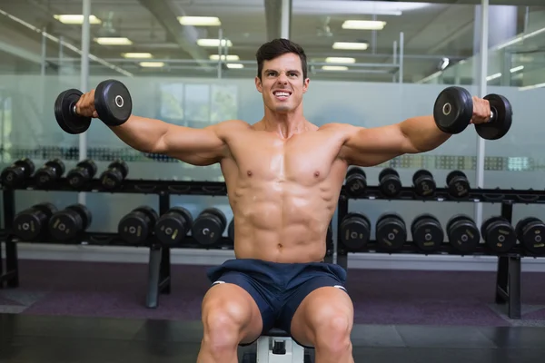 Homem musculoso exercitando com halteres no ginásio — Fotografia de Stock