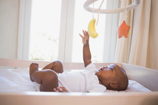 Adorable baby boy lying in his crib playing with mobile — Stock Photo, Image