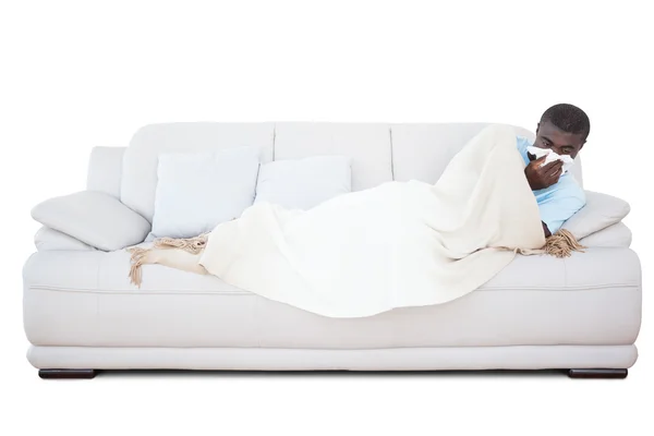 Sjuk man liggande på soffan blåser näsan — Stockfoto