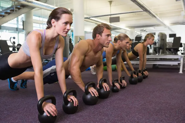 Fitness class in plank position with kettlebells — Stock Photo, Image