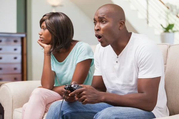 Mujer aburrida sentada junto a su novio jugando videojuegos — Foto de Stock