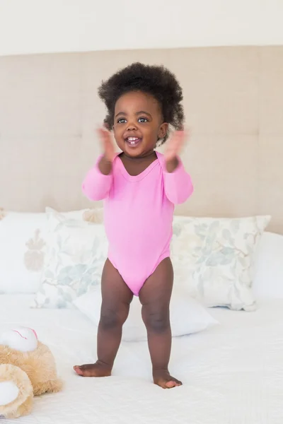 ベッドの上にピンクの babygro 立ってで女の赤ちゃん — ストック写真