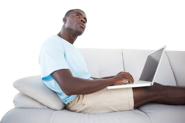 Düşünceli erkek dizüstü kullanarak kanepede oturan — Stok fotoğraf