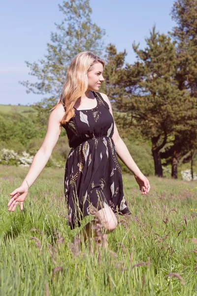 Bonita rubia en vestido de sol caminando por el campo — Foto de Stock