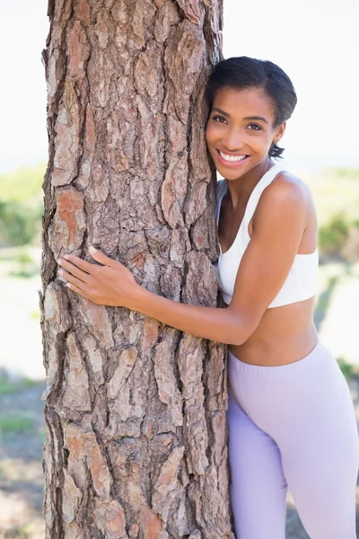 Mujer en forma abrazando un árbol sonriendo a la cámara — Foto de Stock