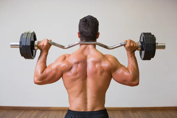 Shirtless muscular man lifting barbell in gym — Stock Photo, Image