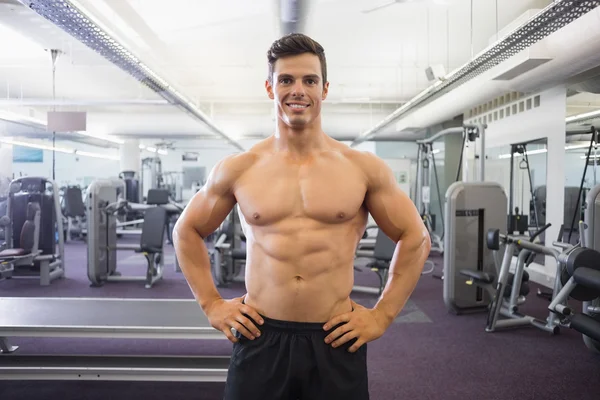 Smiling shirtless muscular man with hands on hips in gym — Stock Photo, Image