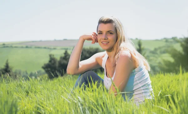 Hezká blondýnka s úsměvem na kameru sedí na trávě — Stock fotografie