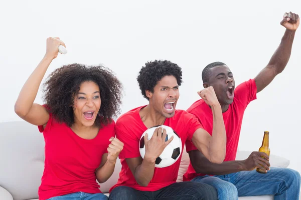 Football fans in red sitting on couch cheering — Stock Photo, Image