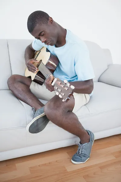 Случайный человек сидит на диване и играет на гитаре — стоковое фото
