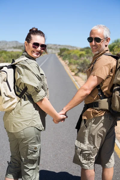 Hitch hiking couple holding hands on the road smiling at camera — Stock Photo, Image