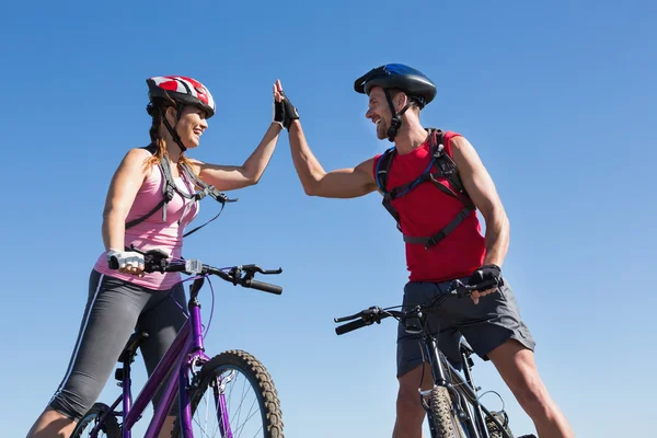 Fit cyclist couple standing at the summit high fiving — Stock Photo, Image