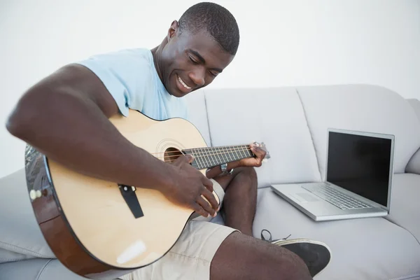 Случайный человек сидит на диване и играет на гитаре с ноутбуком — стоковое фото