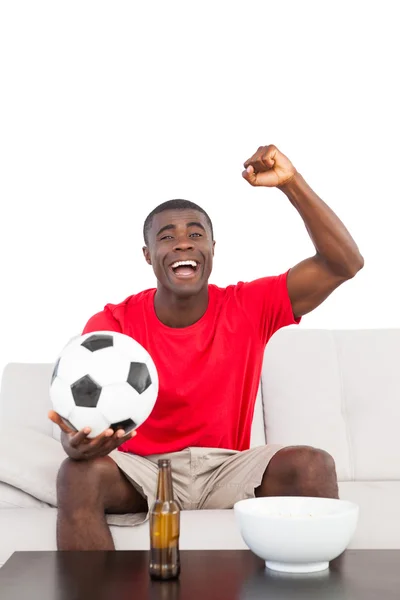 Ventilador de futebol em camisa vermelha sentado no sofá torcendo — Fotografia de Stock