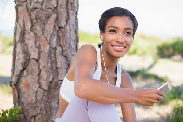 Passar kvinna sitter mot träd, lyssna på musik — Stockfoto