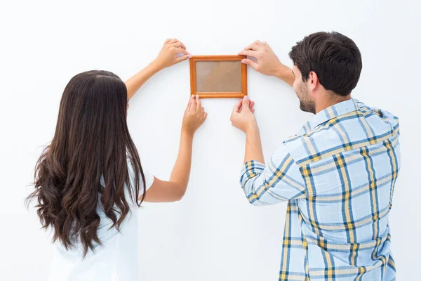 Happy young couple putting up picture frame — Stock Photo, Image