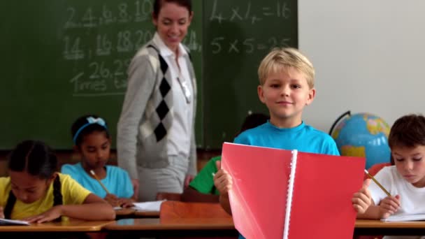 Boy holding red notepad in classroom — Stock Video