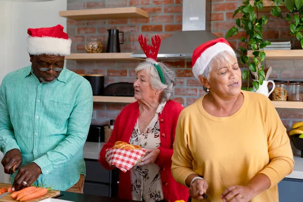 キッチンで一緒に調理クリスマスの帽子の3つの多様なシニア男性と女性の友人 クリスマスのお祝い友達と家でお祝いする — ストック写真