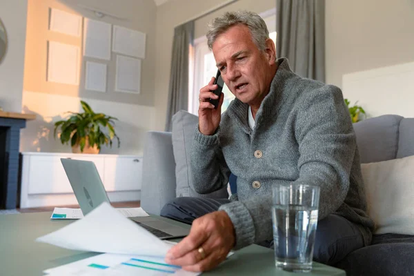 ソファに座って 書類作成 電話をかけ ノートパソコンを使用している白人のシニア男性に焦点を当てました 家庭での積極的な退職生活 — ストック写真
