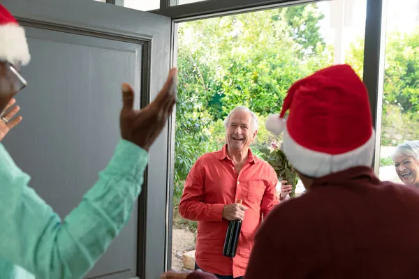 クリスマスの時期には ワインを片手に幸せな白人のシニアカップルがさまざまな友人を訪ねてきます クリスマスのお祝い友達と家でお祝いする — ストック写真