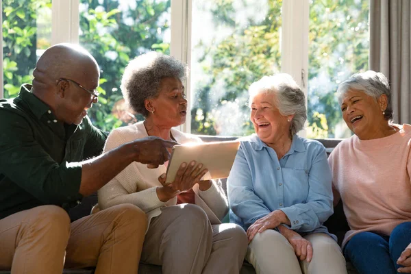 3人の幸せな多様なシニア女性とアフリカ系アメリカ人男性の友人がソファに座ってタブレットを使用しています テクノロジーで自宅でリラックスした退職生活 — ストック写真