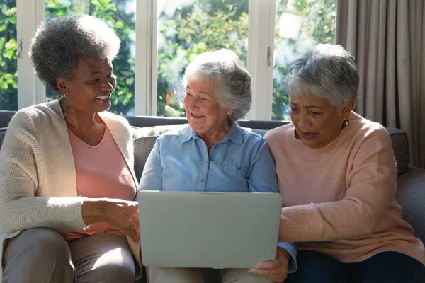 三位快乐多样的老年妇女坐在沙发上 使用笔记本电脑 退休后的生活方式随着科技的进步而放松 — 图库照片