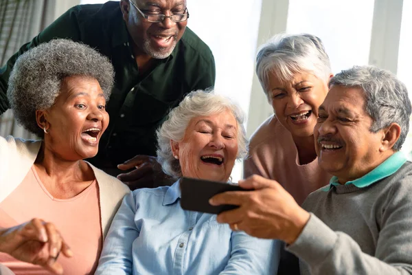 ソファに座ってスマートフォンを見ている5人の幸せな多様なシニア友人 テクノロジーで自宅でリラックスした退職生活 — ストック写真