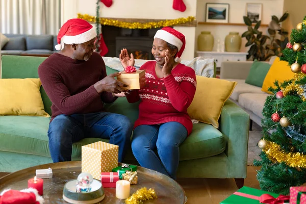 Verrast Afrikaans Amerikaans Seniorenpaar Met Kerstmutsen Die Cadeautjes Delen Met — Stockfoto