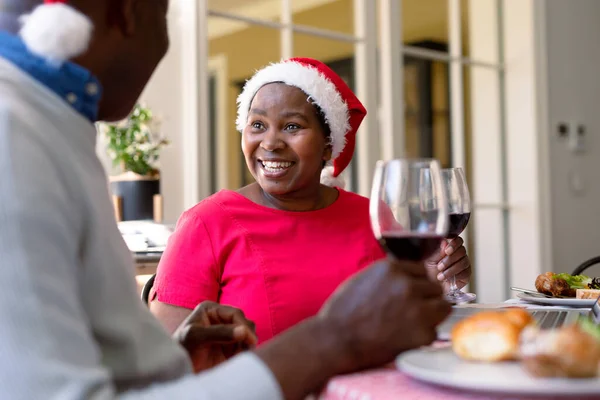 クリスマスの時間にワインとトーストを作るサンタの帽子の幸せなアフリカ系アメリカ人のシニアカップル 引退生活やクリスマスのお祭りを自宅で祝い — ストック写真