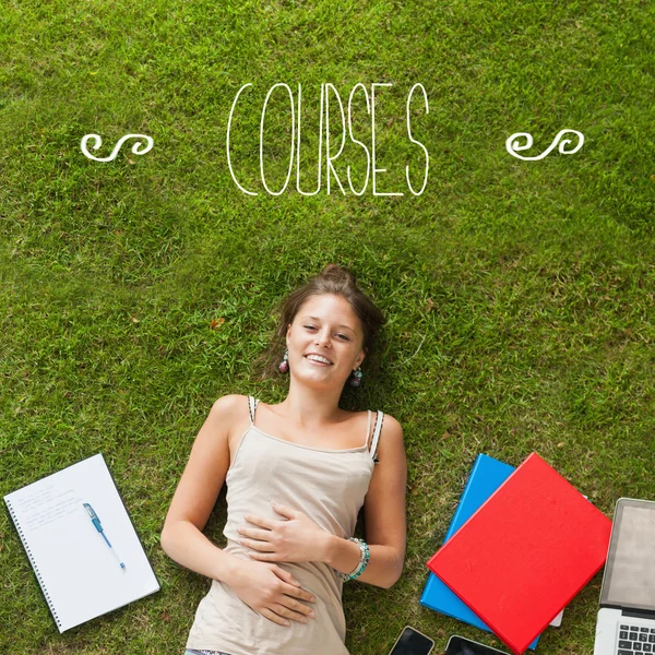 Cursussen tegen mooie student liggen op gras — Stockfoto