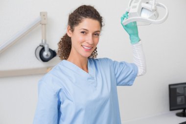 Dentist in blue scrubs smiling at camera beside light clipart