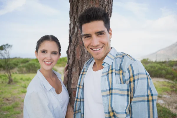 Casal sorridente em pé junto ao tronco da árvore — Fotografia de Stock