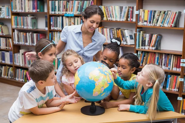 Leerlingen en leraar kijken naar globe in bibliotheek — Stockfoto