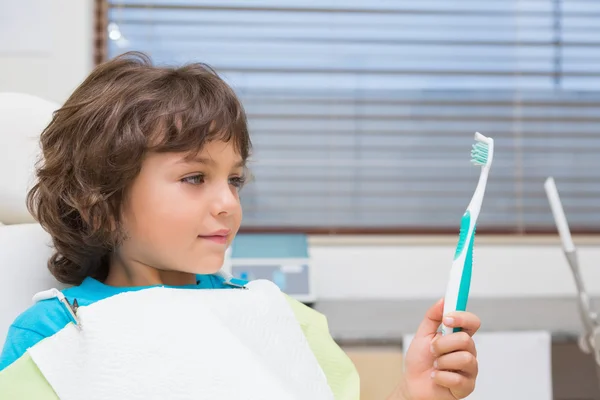 Malý chlapec v zubní křeslo drží toothrbrush — Stock fotografie