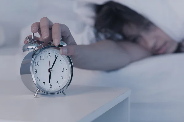 Beautiful brunette hitting alarm clock from under duvet — Stock Photo, Image