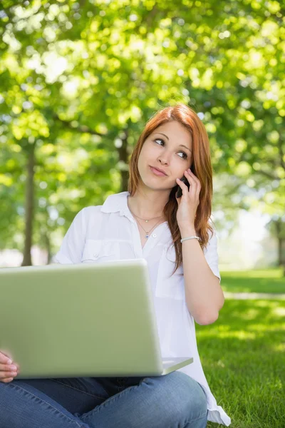 Redhead met behulp van haar laptop tijdens het telefoneren — Stockfoto