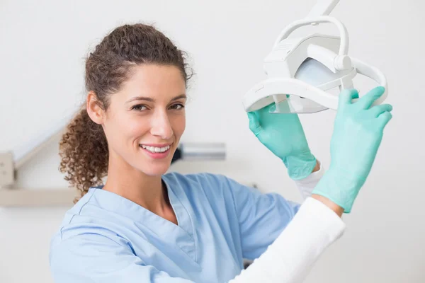 Dentista em azul esfrega sorrindo para a câmera ao lado da luz — Fotografia de Stock