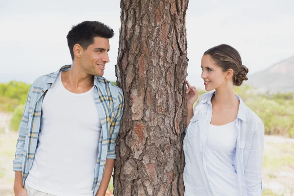 Pareja sonriente parada junto al tronco del árbol — Foto de Stock