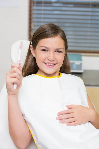 Girl holding toothbrush in dentists chair — Stock Photo, Image