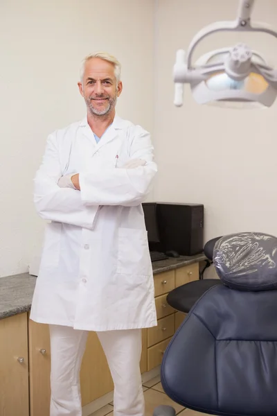 Dentista sonriendo a la cámara junto a la silla — Foto de Stock