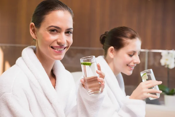 Lächelnde Frauen in Bademänteln, die Wasser trinken — Stockfoto