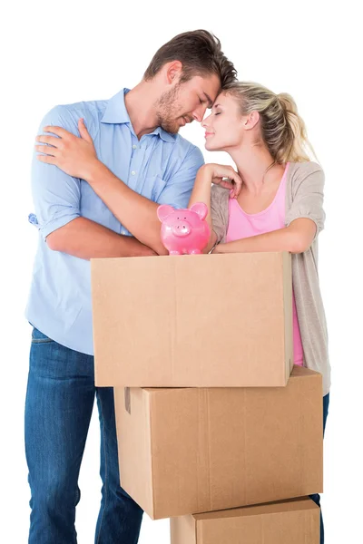 Attractive young couple leaning on boxes with piggy bank — Stock Photo, Image