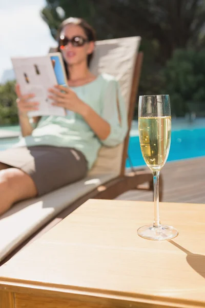 Kvinna läser bok av pool med champagne i förgrunden — Stockfoto